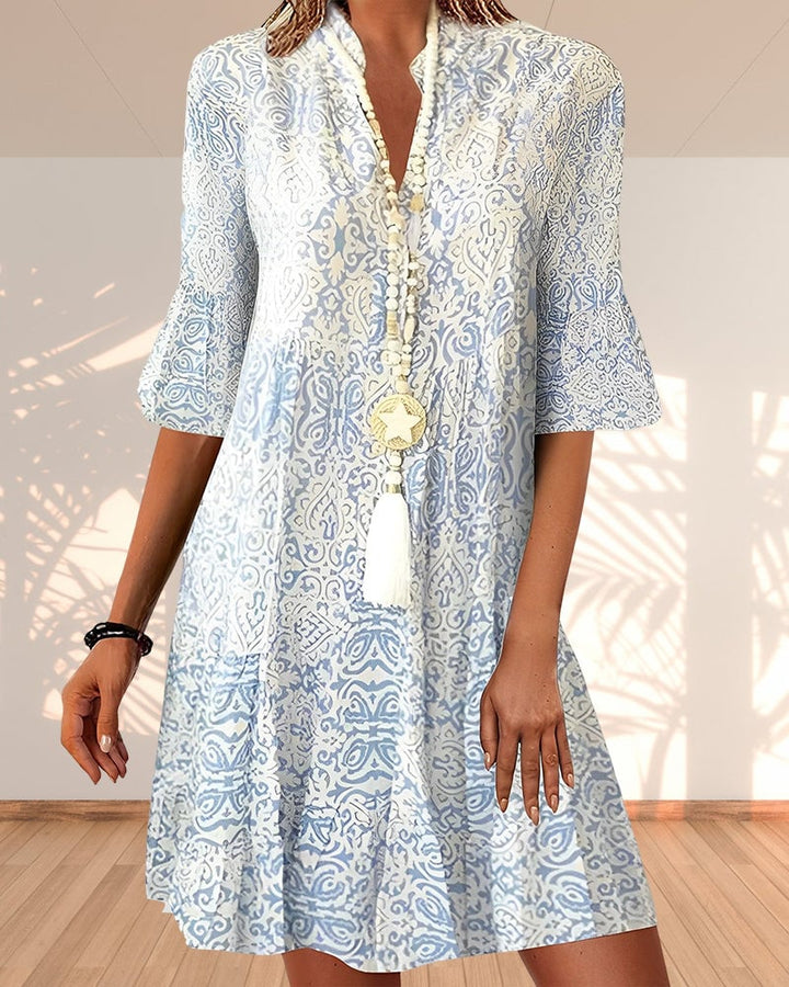 Woman wearing a blue and white paisley floral print V-neck dress with 3/4 bell sleeves and a relaxed fit
