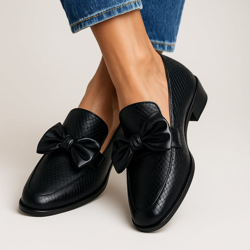 Black bow loafers with a delicate bow accent and sleek silhouette, shown from a front angle