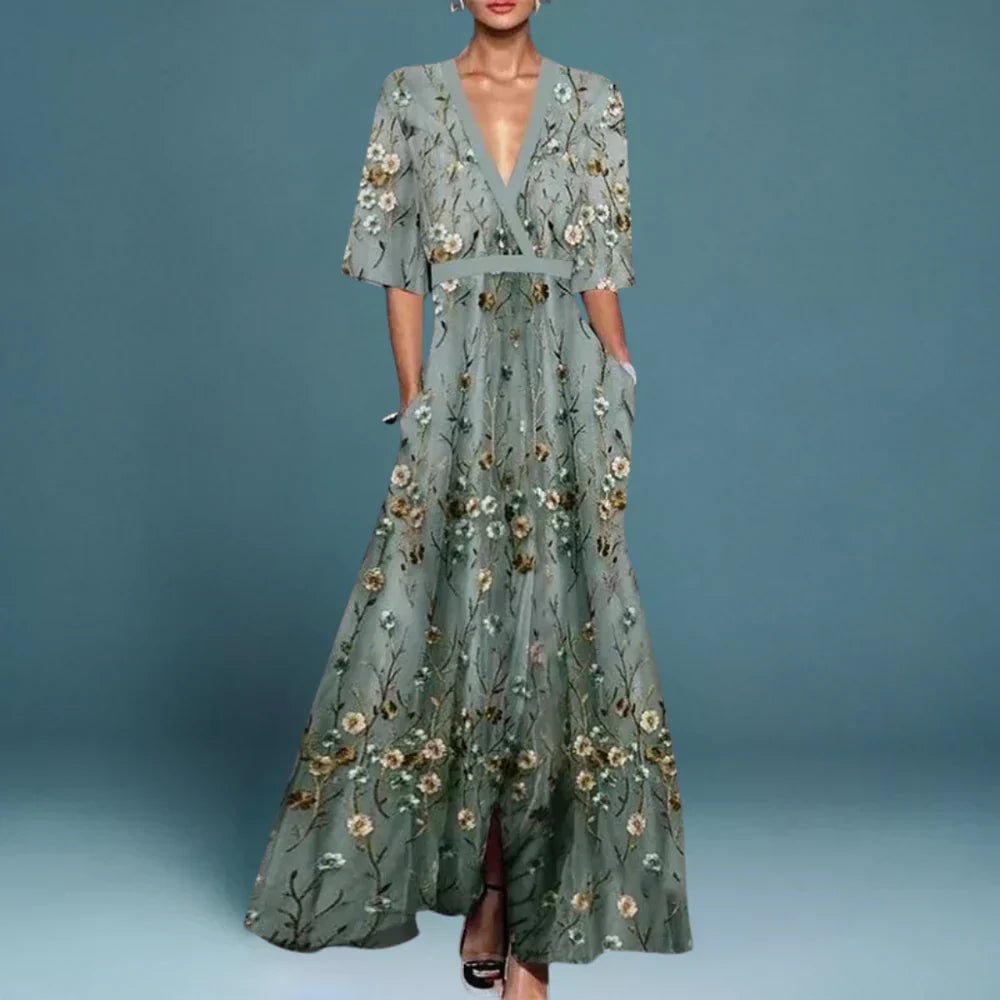 Woman wearing a flowing blue floral maxi dress, standing in a bright outdoor setting with a relaxed, elegant pose