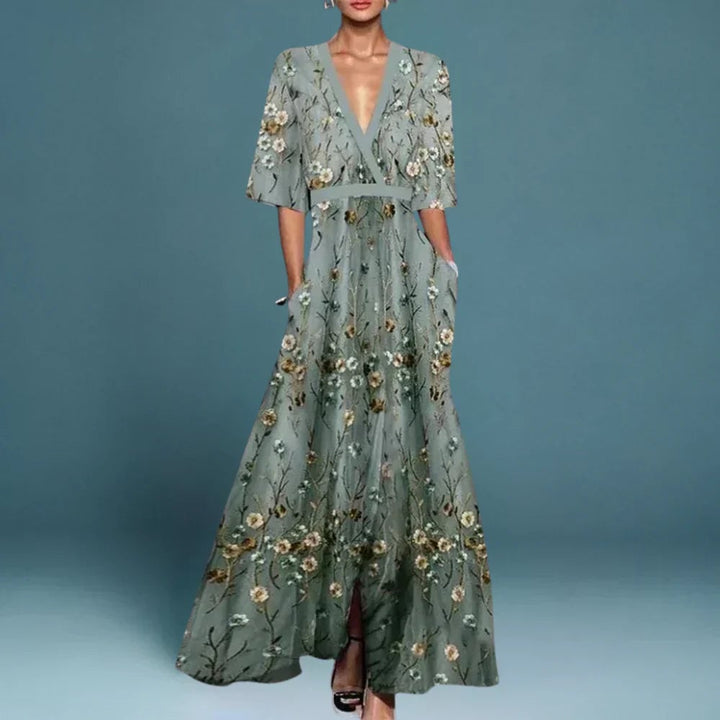 Woman wearing a flowing blue floral maxi dress, standing in a bright outdoor setting with a relaxed, elegant pose