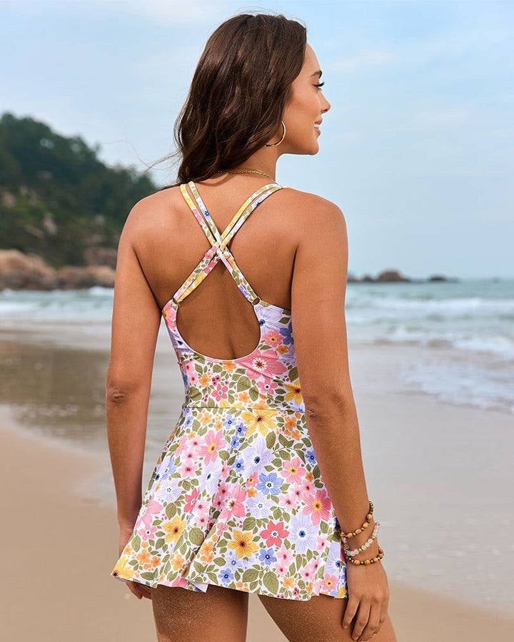 Model in blue-pink floral swim dress walking along the shoreline, skirted overlay flowing