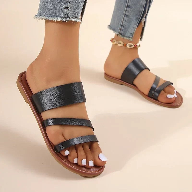 Lilac women's flat sandals in black, angled front view highlighting minimalist strap design