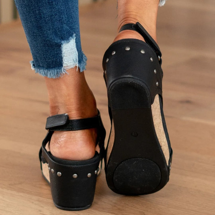 Linda black wedge sandals flat lay on white surface with summer accessories