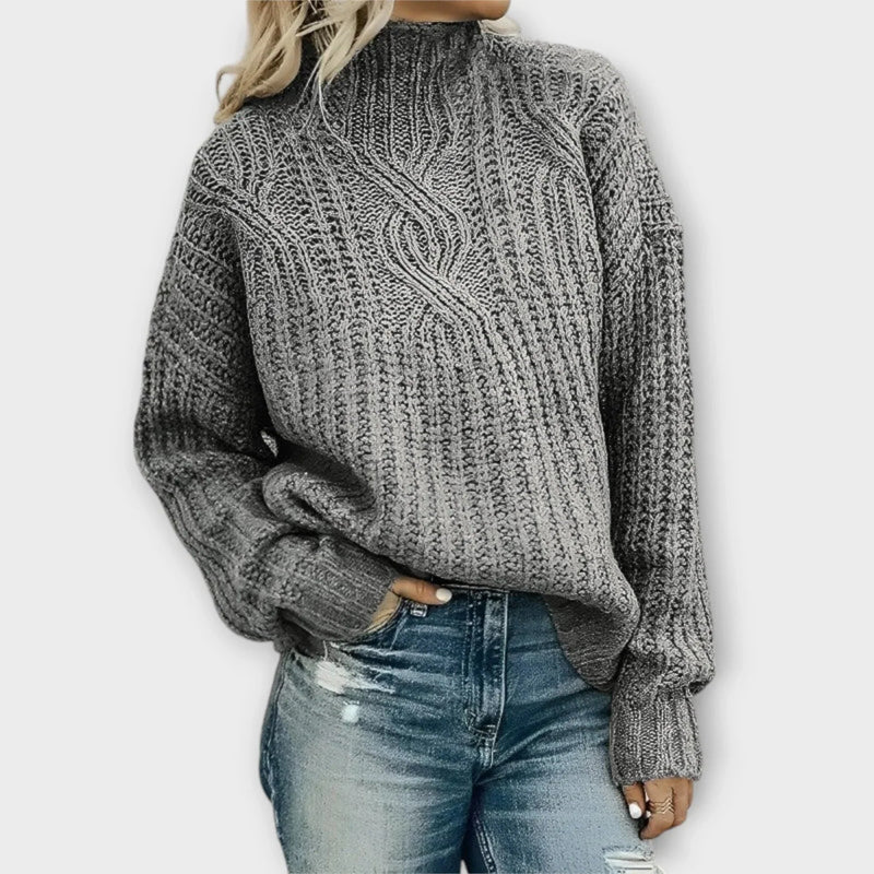 Front view of a modern cable-knit high-neck sweater showing relaxed silhouette and mock-neck detail