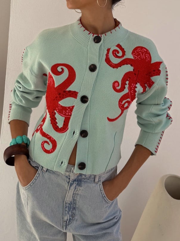 Front view of a mint green cardigan featuring a bold red octopus pattern, shown on a model