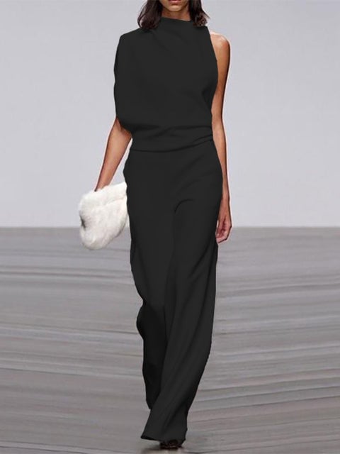 Woman wearing a black one-shoulder wide-leg jumpsuit with a gathered shoulder drape, full-length front view