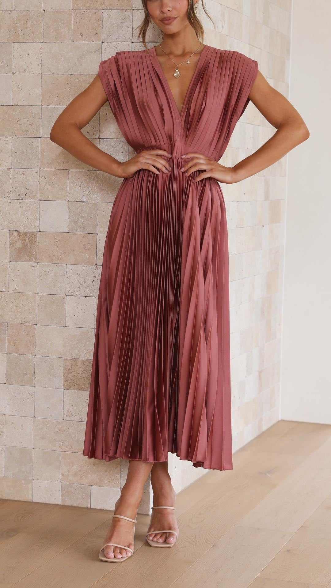 Model wearing an elegant pleated maxi dress in antique pink with a draped V-neckline and flowing high-waisted skirt