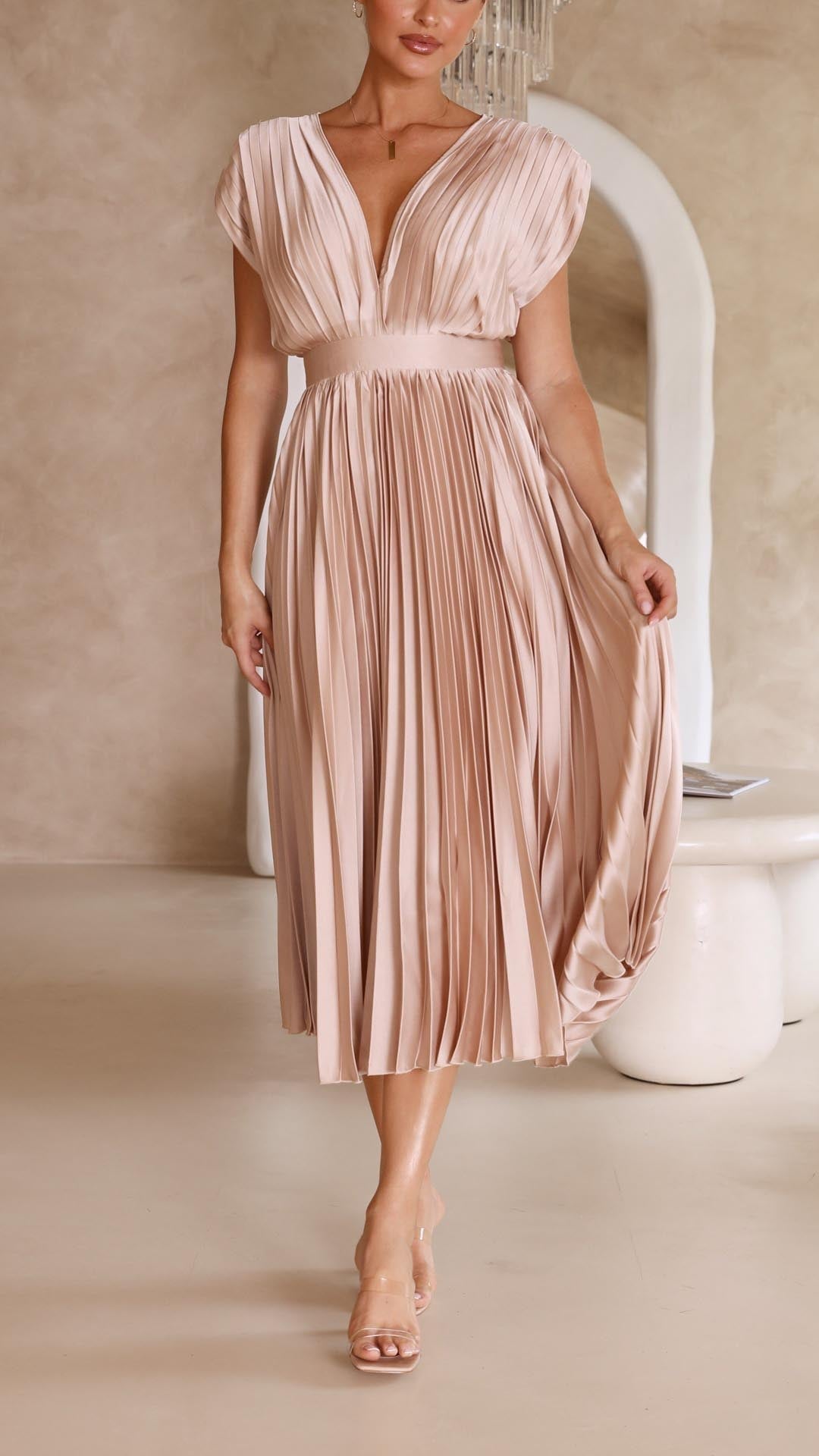 Model wearing elegant pleated maxi dress in champagne color with flowing pleated skirt