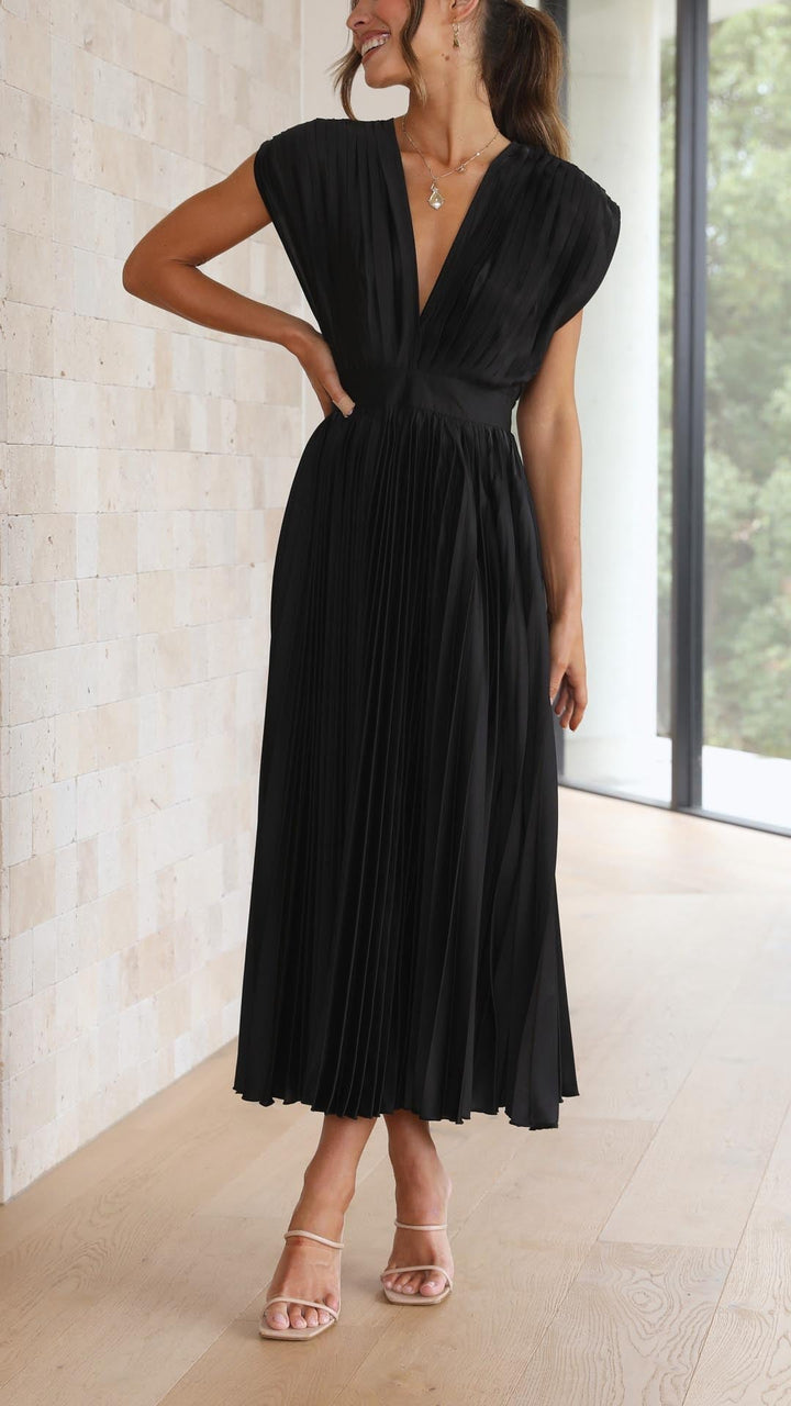 Side profile of model in black pleated maxi dress showing high-waisted fit