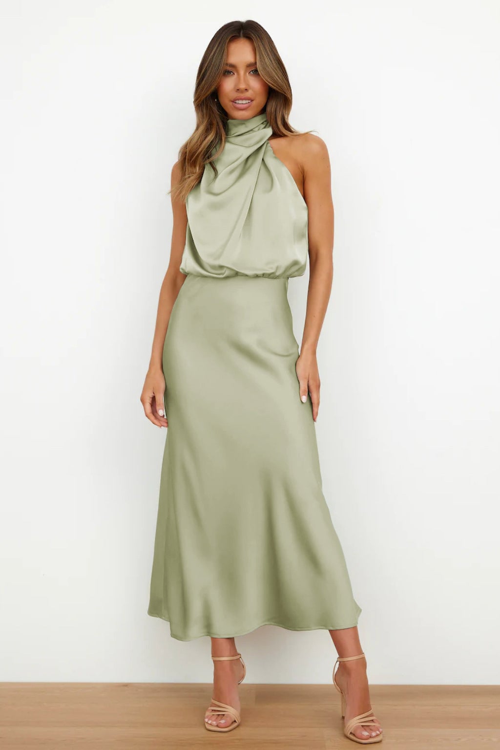 Model wearing a light green satin halter evening dress with a flowing silhouette and high halter neckline