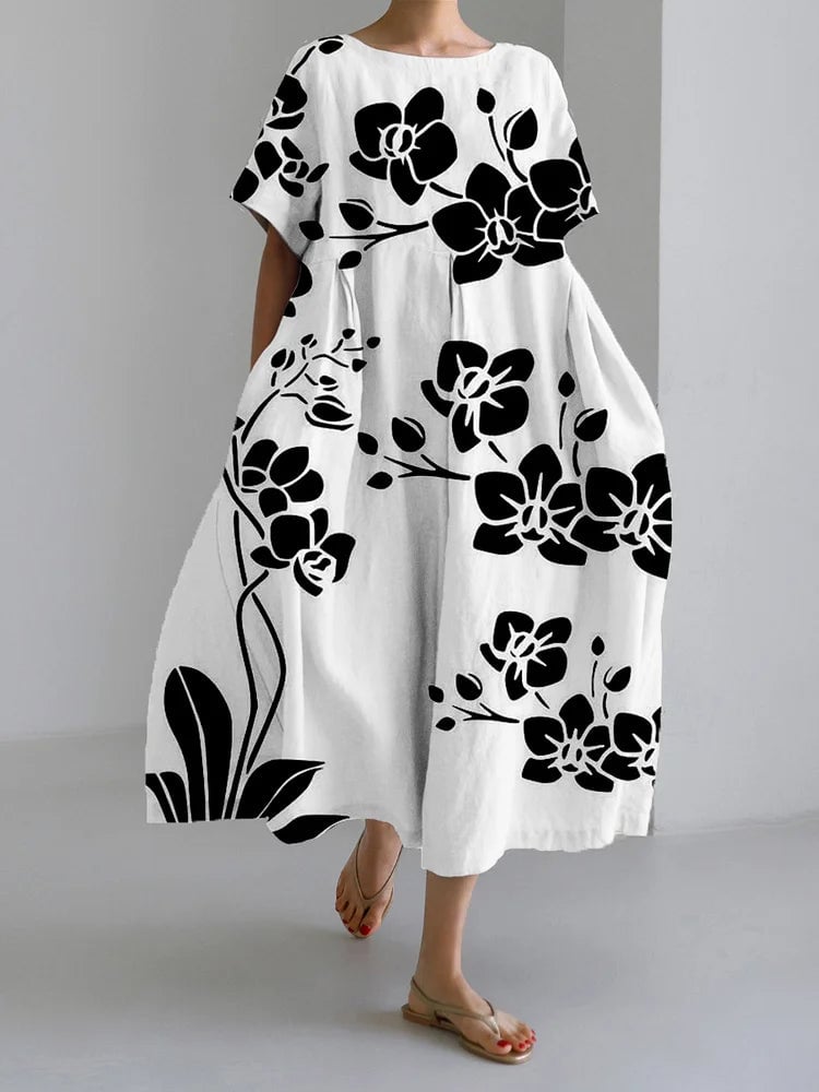 Woman wearing the Marisella white midi dress with black floral print, featuring flowing pleats and a relaxed silhouette