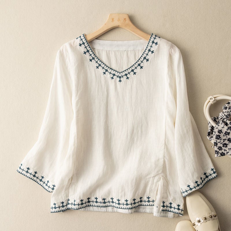 Woman wearing a white embroidered V-neck blouse with delicate stitching along the neckline and cuffs
