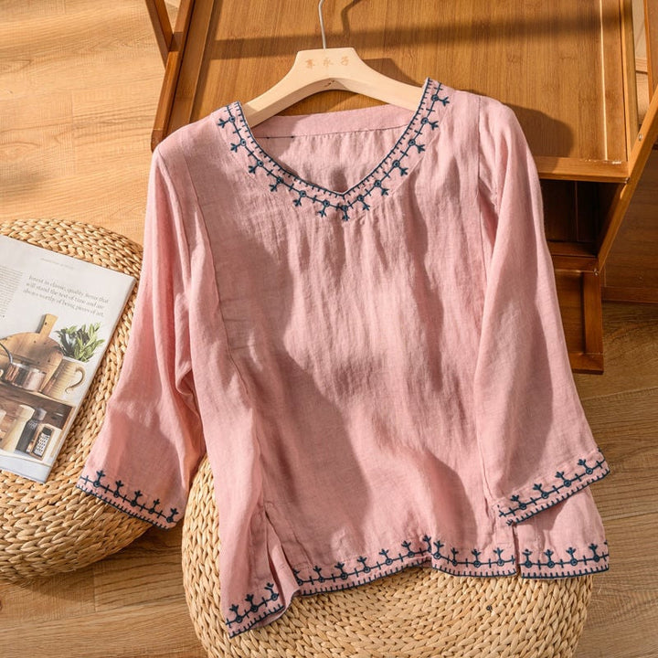 Close-up of embroidered hem and neckline detail on a lightweight V-neck blouse in white