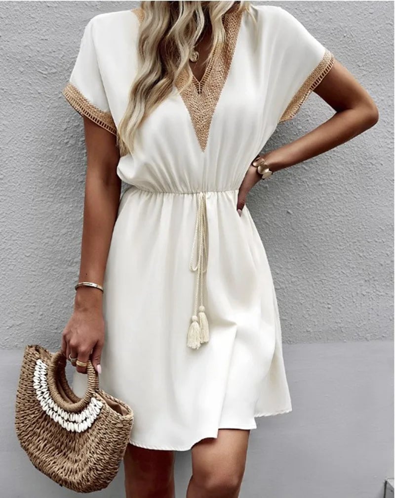 Woman wearing a white boho flowy V-neck draped dress with an adjustable waist tie, front view