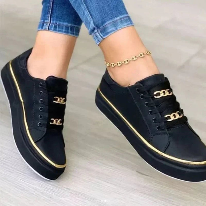 Women's black platform sneakers with gold chain tongue detail and gold-trimmed chunky white sole, front view