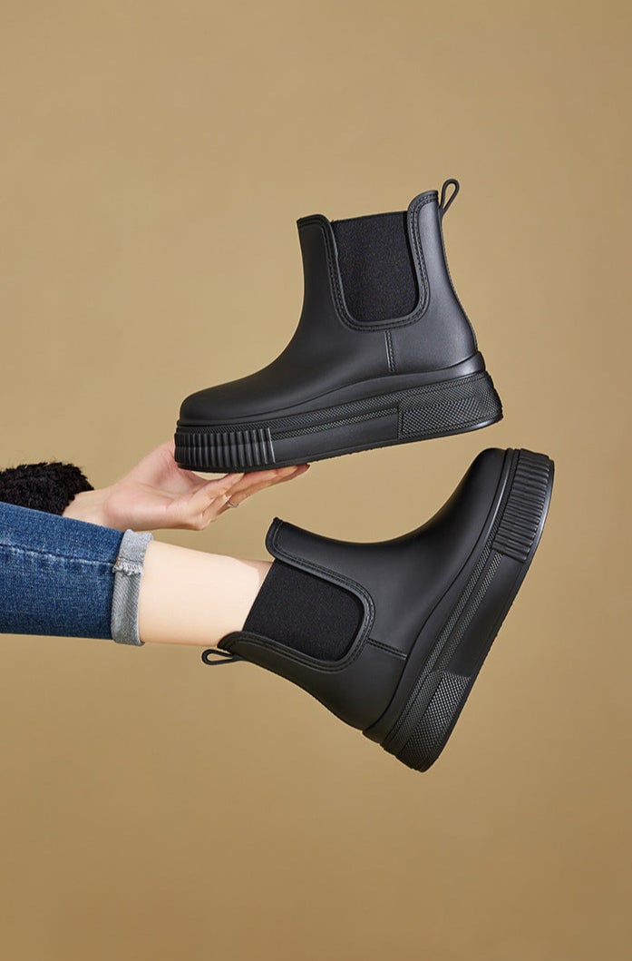 Model wearing Mona rain boots in black with a trench coat and midi skirt