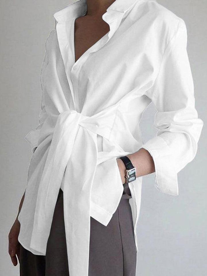 Woman wearing a white tie waist longline button-down blouse with a self-tie knot at the waist