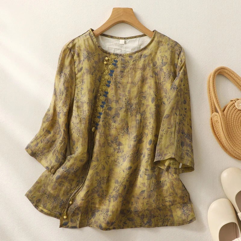 Woman wearing a relaxed floral embroidered blouse with sheer panel accents in green, styled with tailored trousers