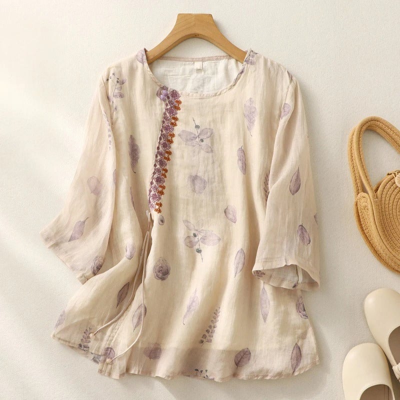Lifestyle flat lay of a floral embroidered relaxed blouse in cream alongside neutral accessories