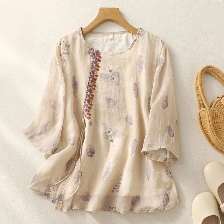 Lifestyle flat lay of a floral embroidered relaxed blouse in cream alongside neutral accessories