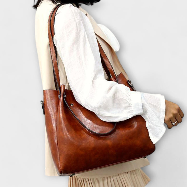 Model carrying the Olivia shoulder bag in brown over her shoulder in an outdoor setting