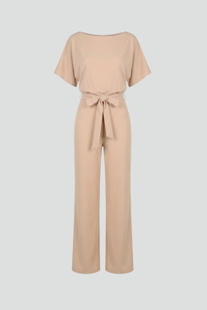 Woman wearing a beige wide leg short sleeve jumpsuit with a tie belt, front view