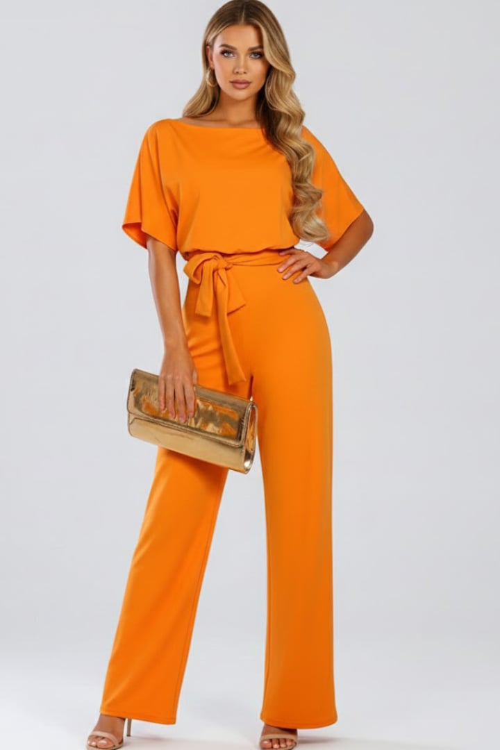 Woman wearing pink wide leg short sleeve jumpsuit with tie belt, full length view