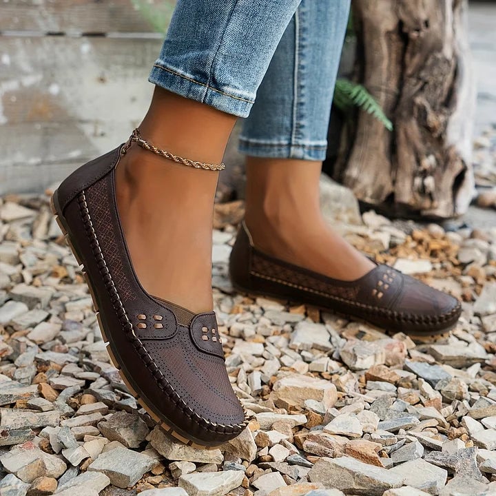 Paulette flats in coffee color shown on a woman standing on pavement, close-up of feet