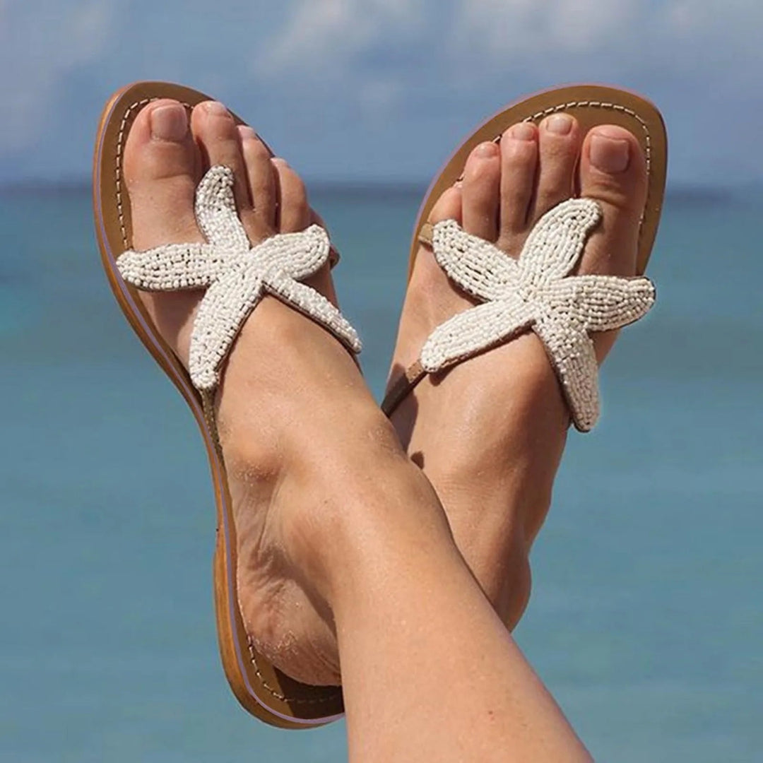 Pair of Primrose slides in silver styled on a sandy beach setting