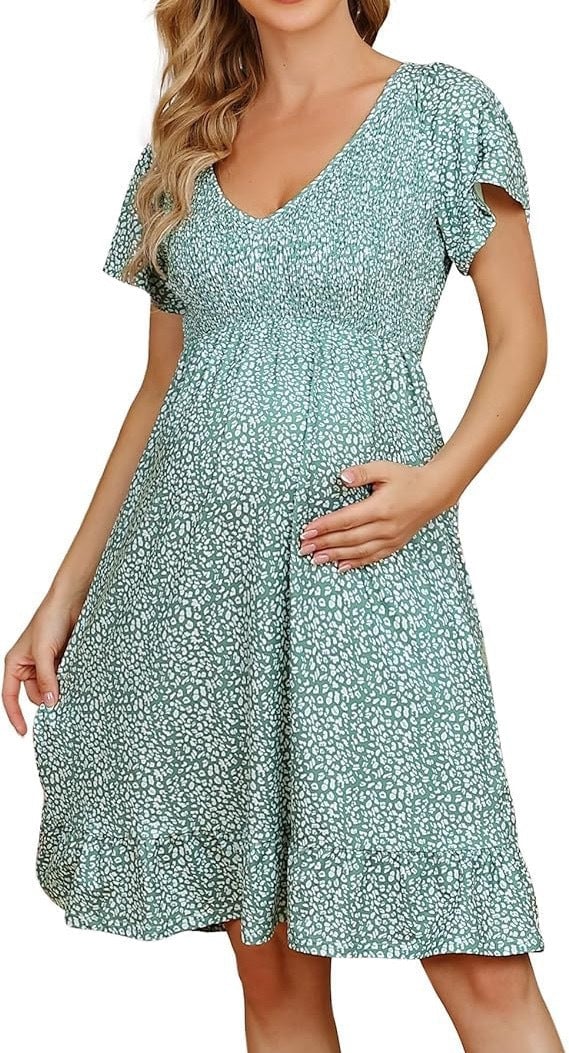 Pregnant model smiling in the Rosalind empire waist dress in sky blue, shown in an outdoor setting