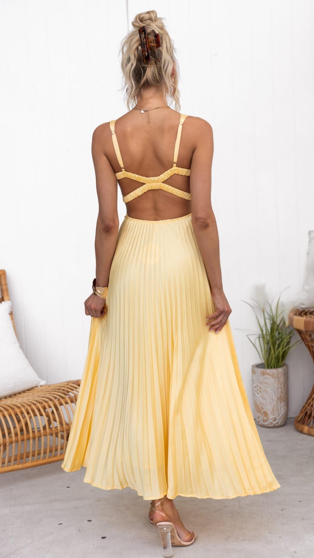 Full-length lifestyle shot of a woman in a yellow pleated V-neck maxi dress at an outdoor event