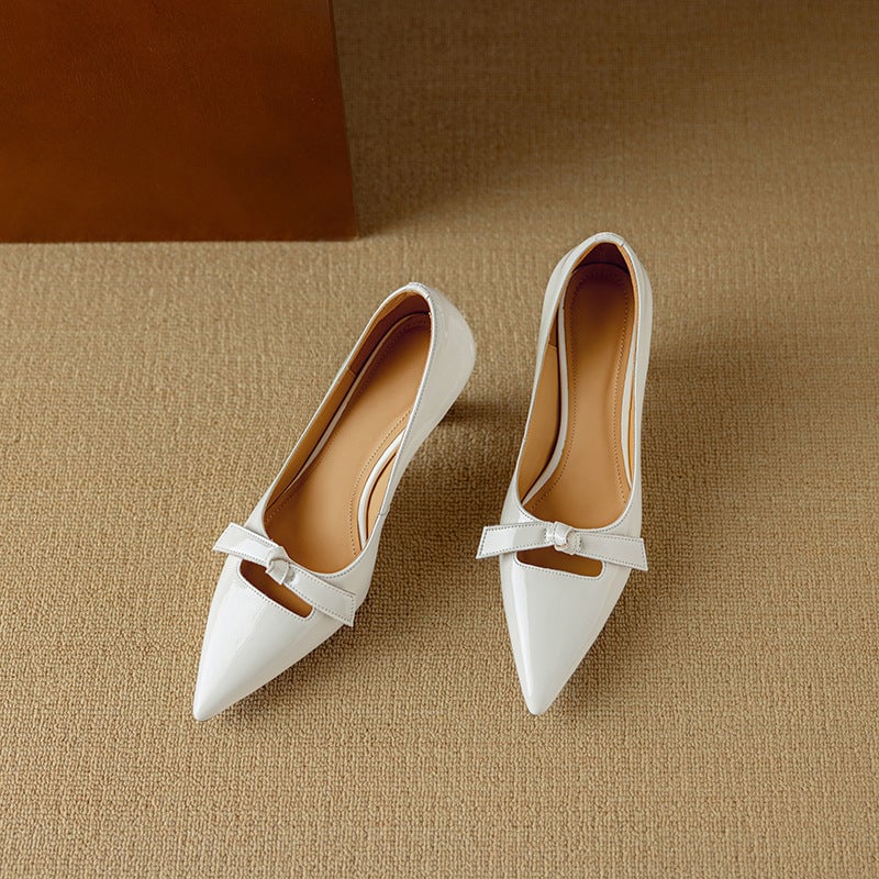 Pair of Rosalind white bow pumps on flat surface, angled view