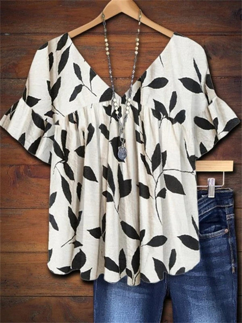 Woman wearing a white leaf print short sleeve blouse with a v-neckline and relaxed gathered fit