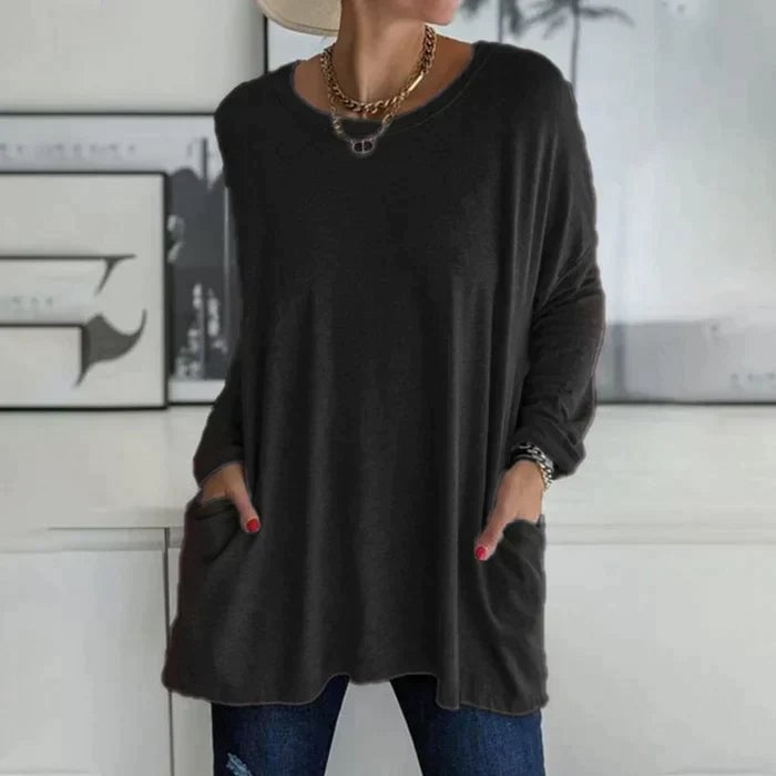 Woman wearing a black oversized long sleeve tunic top with front patch pockets and a relaxed drop-shoulder fit