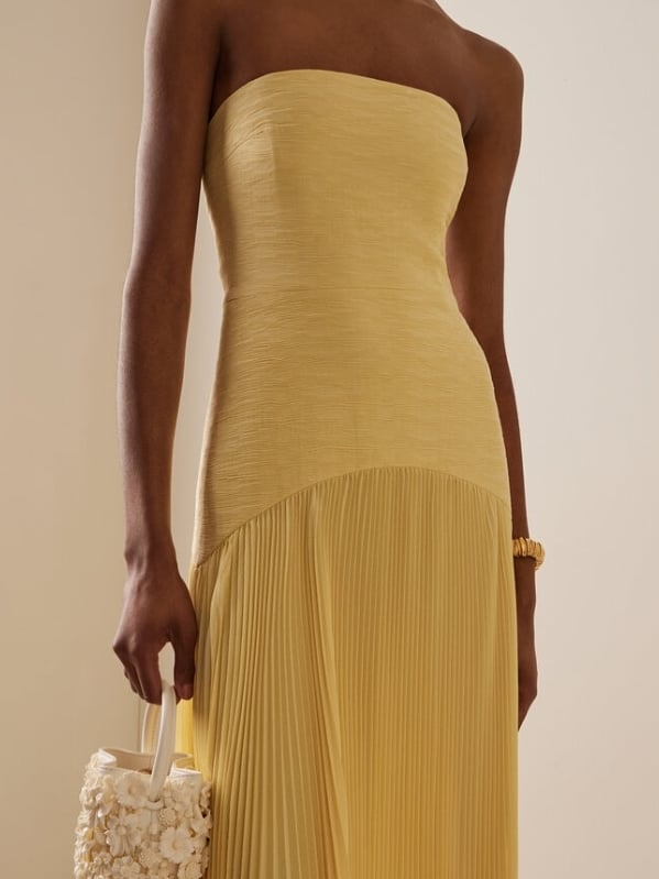 Woman wearing the strapless pleated maxi dress in yellow with a floor-sweeping pleated skirt