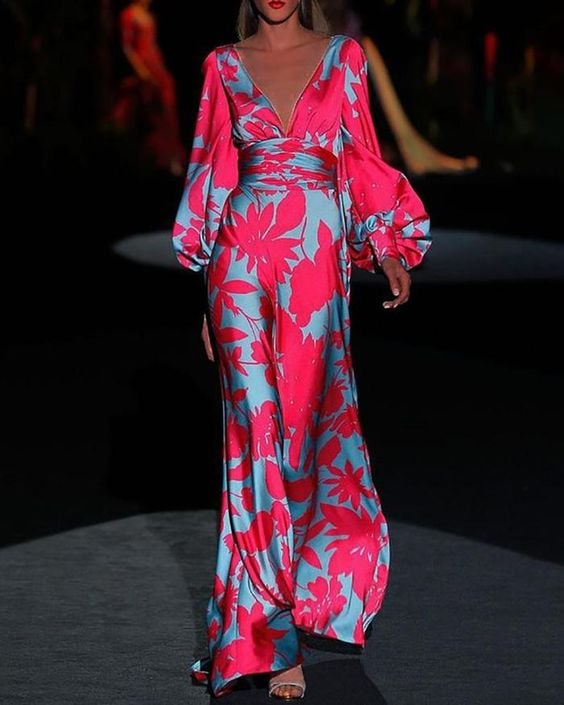 Woman wearing a pink floral satin maxi dress with deep V-neckline and dramatic puff sleeves, floor-length fit