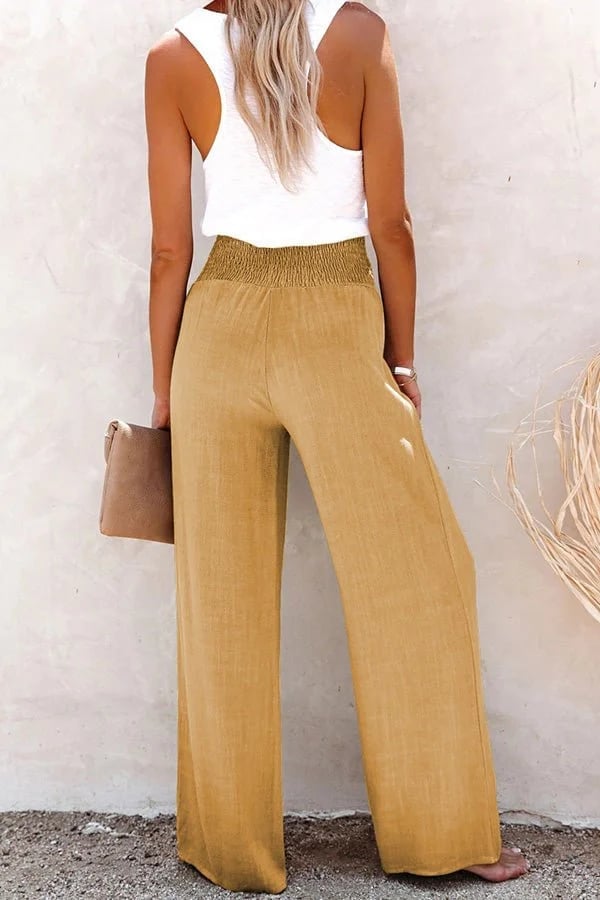 Flat lay of high-waisted trousers showing fabric texture, button accents, and smocked waistband detail