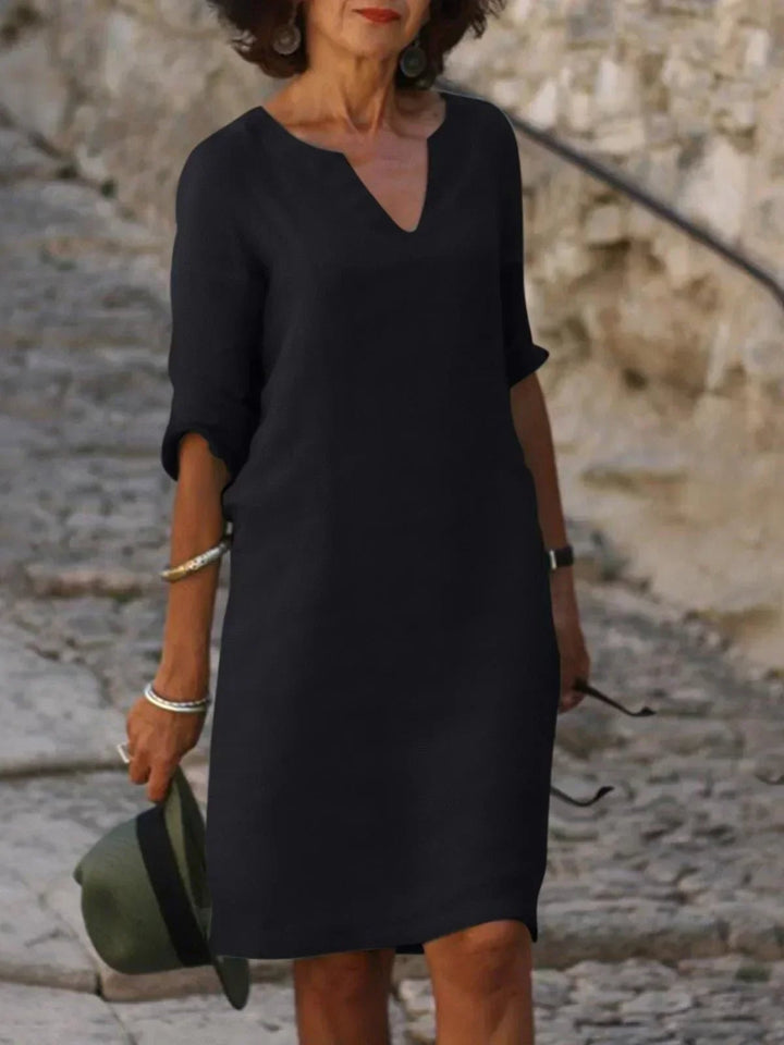 Front view of a flowing V-neck dress in olive green with delicate pleats at the waist