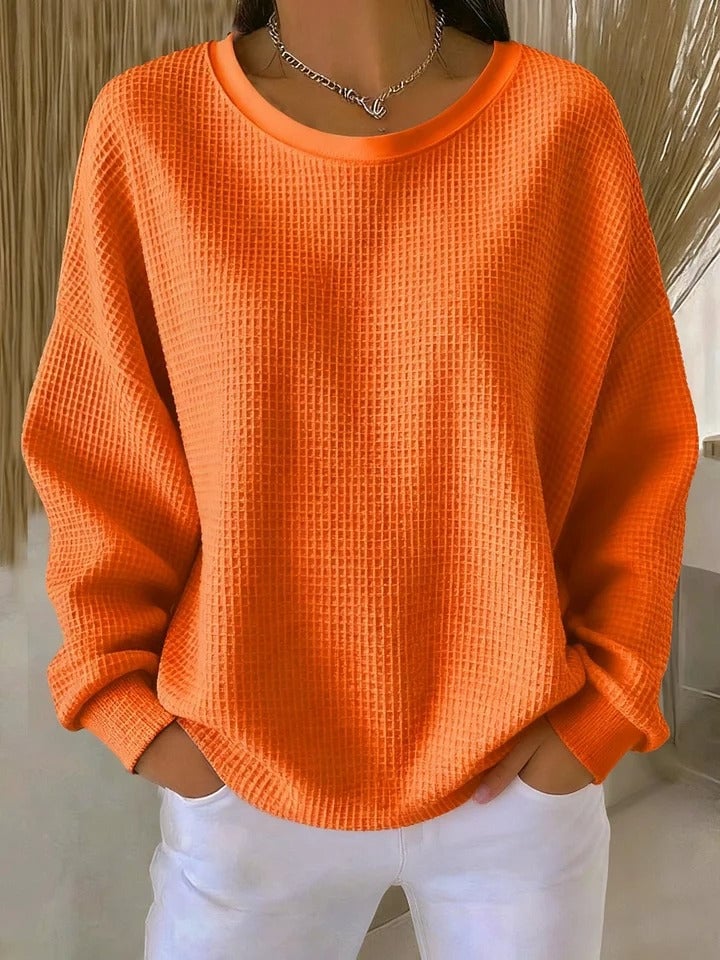 Model wearing the Sofia textured knit sweater in orange, layered under an open coat for a chic cold-weather look