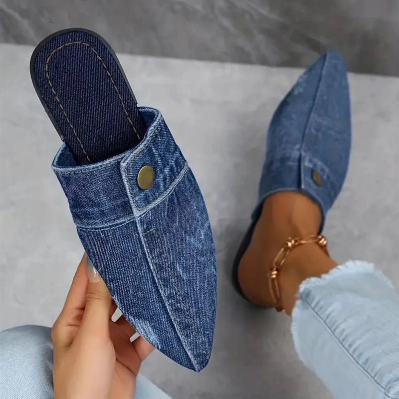 Sofia denim mule flat in indigo, top-down view highlighting pointed toe silhouette and brass button detail