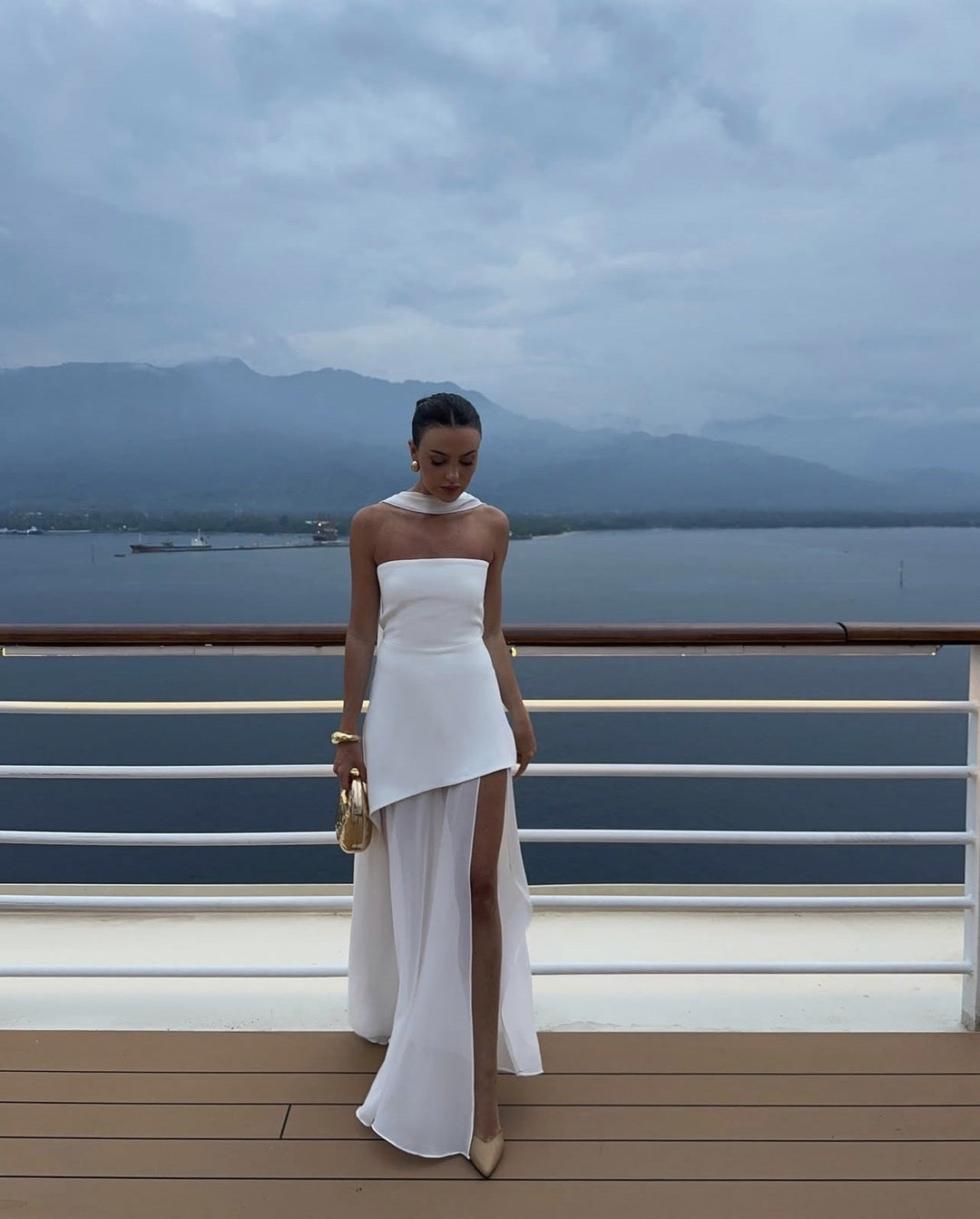 Side profile of woman in the Stella white asymmetric maxi dress highlighting the flowing high-low skirt