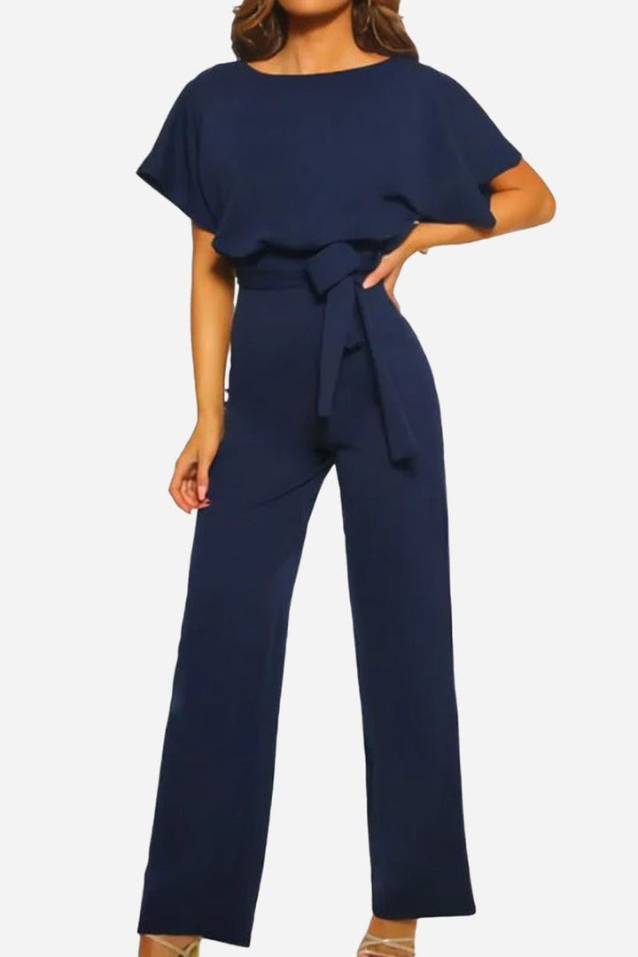 Woman styling the Stella jumpsuit in beige with heeled sandals for a daytime look