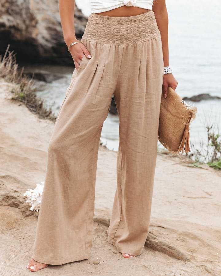Woman wearing flowing wide-leg beach pants in beige with a relaxed fit and gathered waistband, styled for a beach day