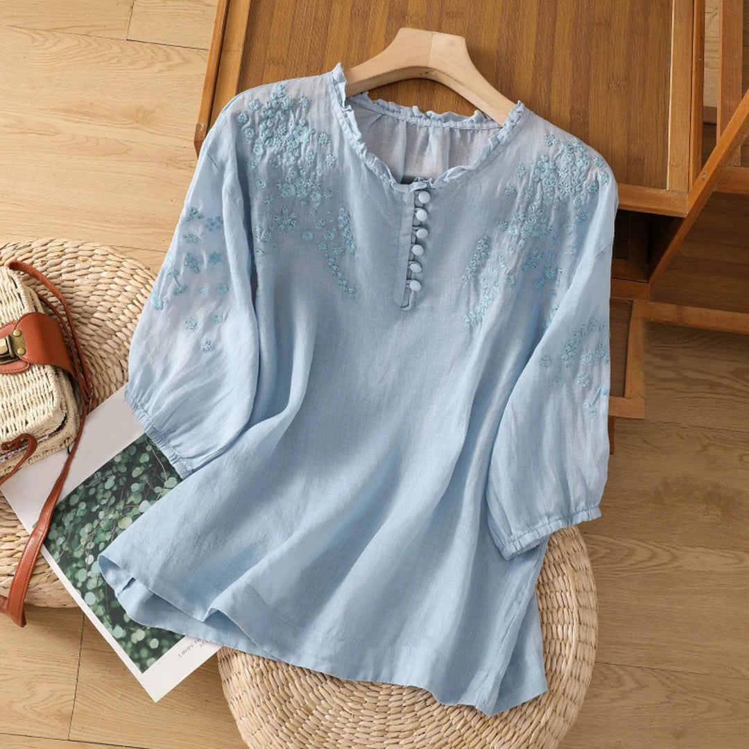 Woman wearing a white floral embroidered button-front blouse with delicate stitching along the neckline