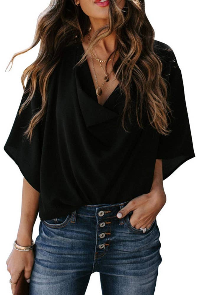 Woman wearing a black draped cowl neck batwing sleeve blouse with a relaxed wrap-style front and tapered wrists