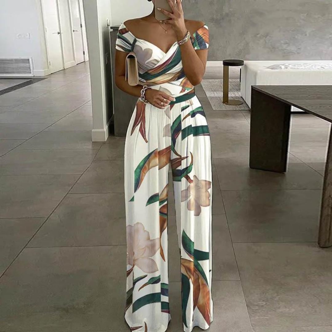 Woman wearing the Vera blue botanical-print wide-leg jumpsuit with off-shoulder wrap bodice and ruched waist detail