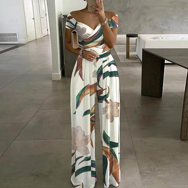 Woman wearing the Vera blue botanical-print wide-leg jumpsuit with off-shoulder wrap bodice and ruched waist detail