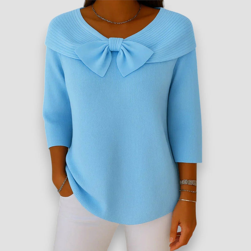 Woman wearing a soft light blue knit sweater with a delicate bow accent at the neckline, relaxed fit, front view