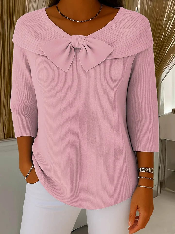 Close-up of the bow detail on a pink knit sweater, highlighting the feminine neckline accent