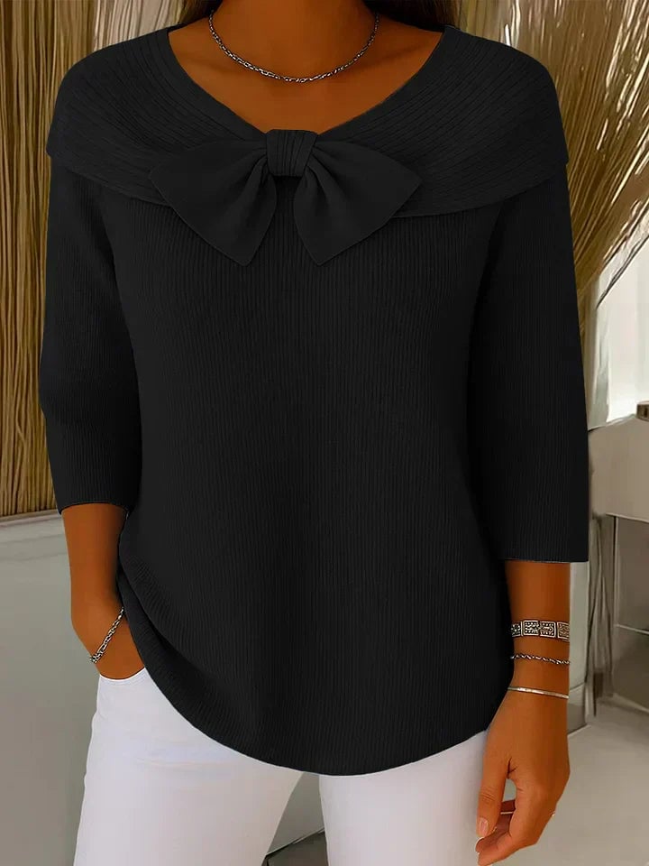 Flatlay of a black knit sweater with bow detail showing the soft fabric texture and relaxed silhouette